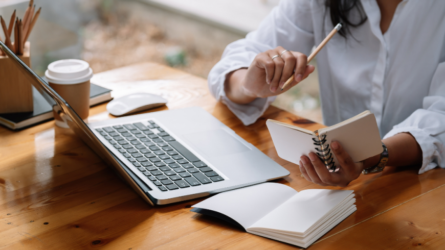 Ragazza al computer con taccuino e penna in mano