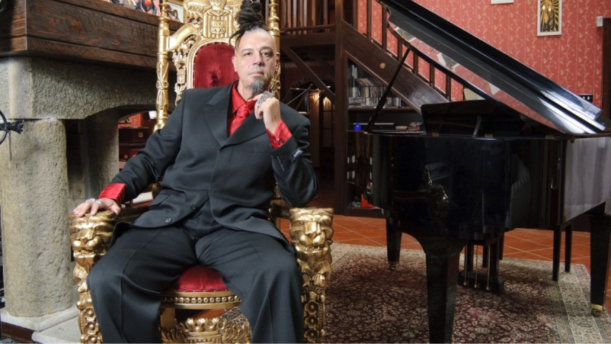 foto di Madaski seduto su una poltrona di fianco ad un pianoforte a coda