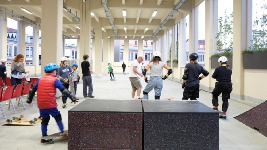 Un gruppo di bambini, ragazzi e adulti partecipa a una lezione o sessione di skateboard e pattinaggio