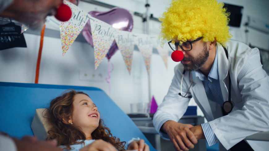 Un medico travestito da clown fa sorridere una bambina ricoverata in un letto d'ospedale addobbato a festa