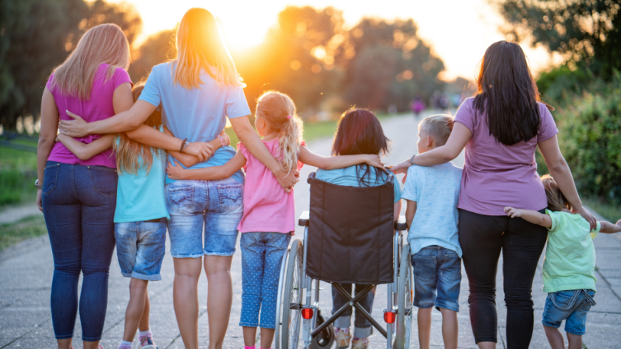 un gruppo di donne e bambini, tra cui una ragazza in sedia a rotelle, che camminano abbracciati di spalle verso il tramonto