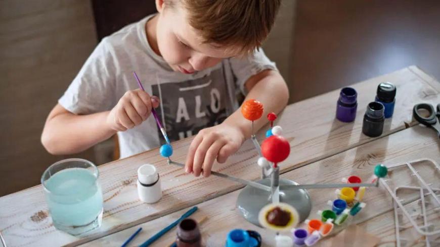 un bambino concentrato a dipingere un modellino del sistema solare da tavolo