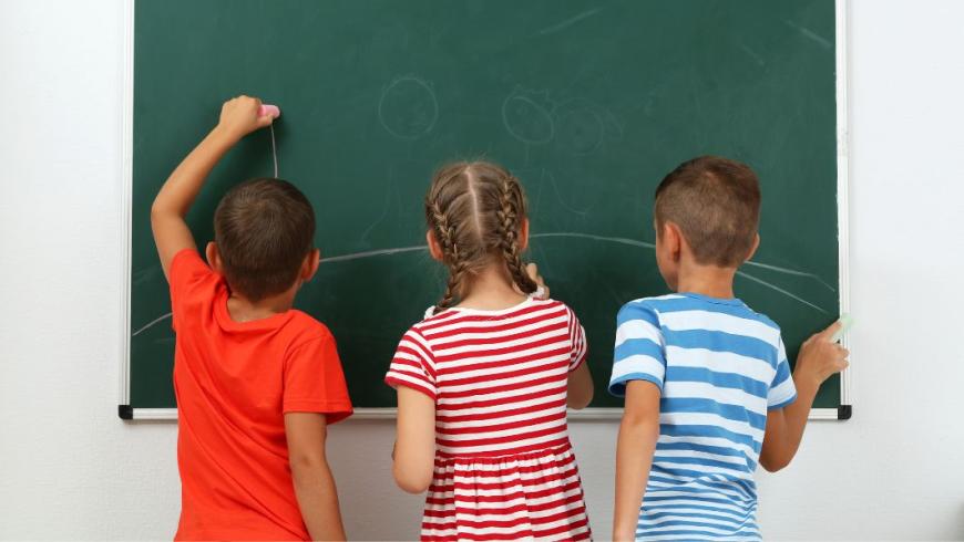 tre bambini di spalle davanti alla lavagna