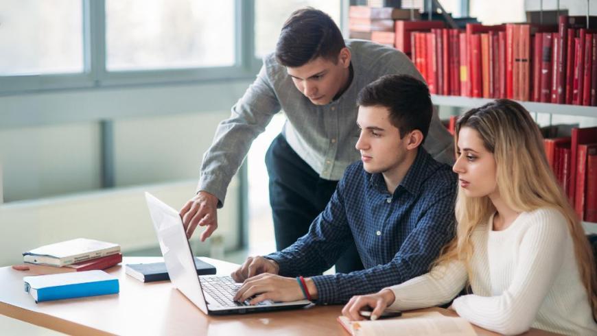 Tre studenti studiano al pc circondati da libri