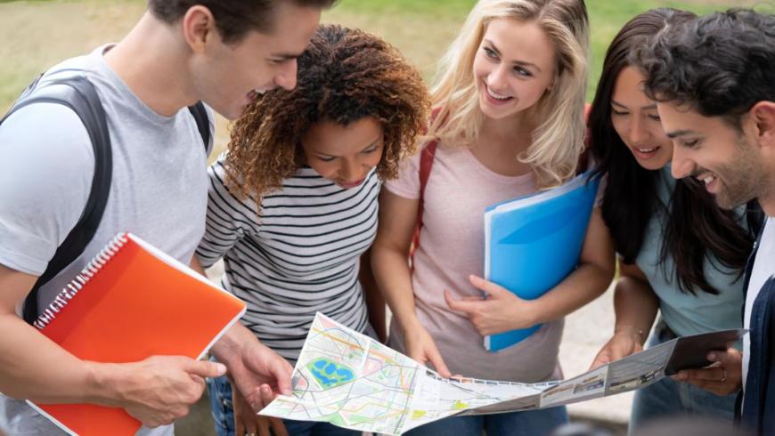 gruppo di ragazze e ragazzi con libri in mano che guardano una cartina