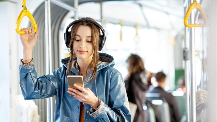 ragazza con le cuffie attaccata alla maniglia del tram guarda lo smartphone